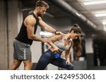 A fit muscular sportswoman is doing kettle bell row in a gym with her instructor.