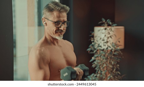 Fit, older shirtless man at home doing workout training exercise in morning by window, showcasing health and vitality, using barbell. - Powered by Shutterstock