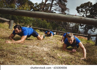 Fit people crawling under the net during obstacle course in bootcamp - Powered by Shutterstock