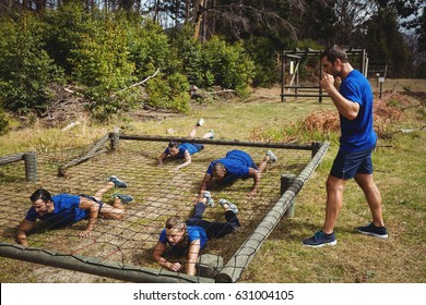 Fit people crawling under the net during obstacle course in bootcamp - Powered by Shutterstock