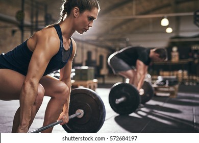 Fit people preparing to deadlift and holding barbells. Horizontal indoors shot