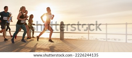 Fit people running a marathon race along a promenade by the ocean. Male and female runners compete in a run and promoting a healthy lifestyle and active lifestyle. Group of runners wearing bibs. 