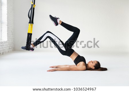 Fit pretty young woman doing fly yoga stretching exercises with trx fitness straps  in fitness training white gym loft classroom. Sport healthy lifestyle concept. Copy space.