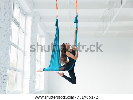 Fit pretty young woman doing fly yoga stretching exercises  in fitness training white gym loft classroom. Sport and healthy lifestyle concept. Copy space, empty space for text.