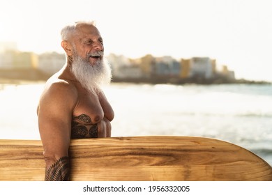 Fit senior male having fun surfing during sunset time - Retired man training with surfboard on the beach - Elderly healthy people lifestyle and extreme sport concept - Powered by Shutterstock