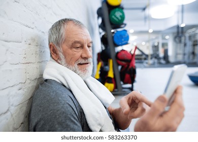 Fit Senior Man In Gym Resting, Holding Smart Phone.