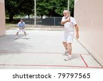 Fit senior man plays raquetball with his adult son.