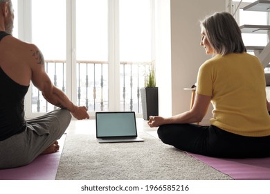 Fit Senior Older Couple Watching Online Yoga Class Doing Virtual Fitness Training Exercises Sitting On Floor At Home Looking At Screen Using Laptop Computer. Meditation With Virtual Coach Instructor.