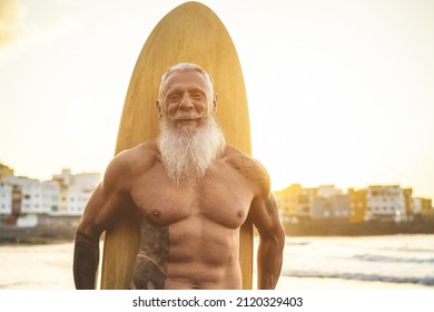 Fit Senior Surfer Holding Vintage Surf Board On The Beach At Sunset - Focus On Face