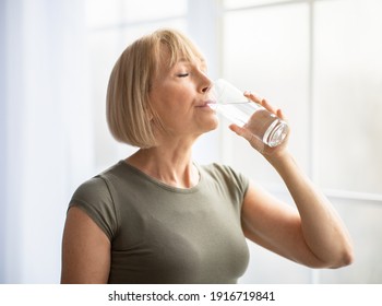 Fit senior woman drinking clear water during her workout break at home. Mature Caucasian lady staying hydrated after sports training. Healthy lifestyle and wellness concept - Powered by Shutterstock