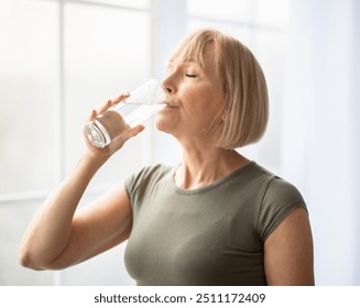 Fit senior woman drinking clear water during her workout break at home. Mature Caucasian lady staying hydrated after sports training. Healthy lifestyle and wellness concept - Powered by Shutterstock