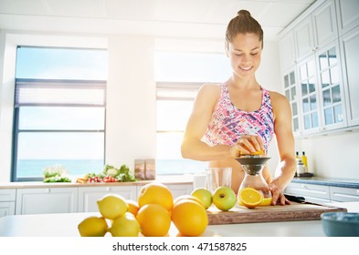 Fit smiling young woman preparing healthy fruit juice from an assortment of fresh fruit using a manual juicer in her kitchen , copy space on a high key window background - Powered by Shutterstock