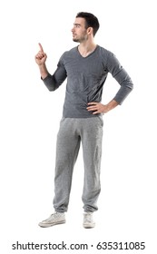 Fit Sport Man In Sweat Pants And Gray Shirt Pointing Finger Up Looking At Copyspace. Full Body Length Portrait Isolated On White Studio Background. 