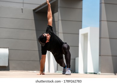 Fit sports man warming up with spider lunge exercise outdoors on building rooftop floor