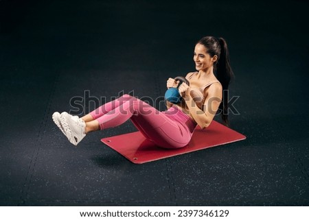 A fit sportswoman is doing kettlebell russian twist on a exercise mat in a gym.