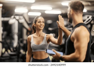 Fit sportswoman giving high five to her fitness instructor at gym.