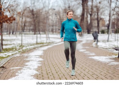 Fit sportswoman jogging on path in park on snowy winter day. Recreation, snowy weather, winter day - Powered by Shutterstock