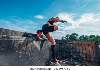 Fit sportswoman participating in an physically demanding obstacle course race and overcoming one of the obstacles. OCR race concept. Focus on a woman legs while jumping over the fence. - Powered by Shutterstock