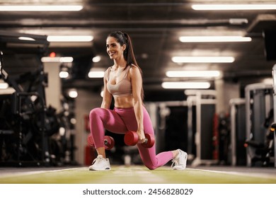 A fit sportswoman in shape is practicing with dumbbells and doing lunges in a gym. - Powered by Shutterstock