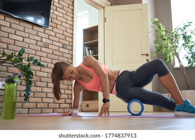 Fit Sporty Woman Wearing Sportswear Roll On Foam Massage Roller Massaging Leg Muscle Lying On Yoga Mat Floor At Home. Active Young Girl Doing Fitness Workout Training Exercise In Apartment Living Room