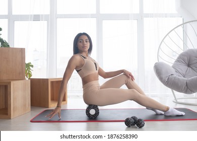 Fit Sporty Woman Wearing Sportswear Roll On Foam Massage Roller Massaging Leg Muscle Lying On Yoga Mat Floor At Home. Active African Girl Doing Fitness Workout Training Exercise In  Living Room.