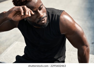 Fit sporty young African man wearing black sportswear relaxing after workout in urban park on summer day. Strong muscular guy bodybuilder sweating, sport street training outdoors, closeup. - Powered by Shutterstock