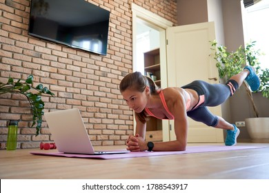 Fit sporty young woman doing plank online workout exercise at home. Active healthy girl enjoy sport pilates yoga fitness training on laptop computer stretching on yoga mat watching video class.