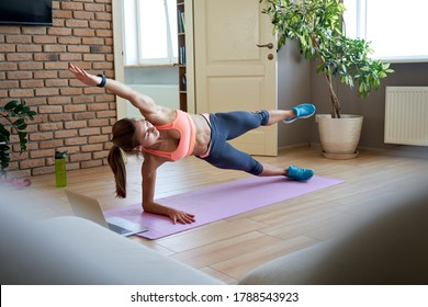 Fit sporty young woman doing side plank online workout exercise at home. Active girl learning sport pilates yoga fitness training live stream video tutorial class on laptop computer online on yoga mat