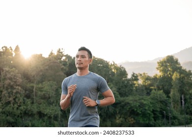 A fit and strong Asian man in sportswear is running on the street in a park in the morning. exercise, workout, marathon - Powered by Shutterstock