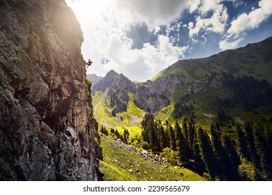 Fit strong man athlete in silhouette rock climbing on the high vertical wall at the mountains Tyan Shan in Kazakhstan