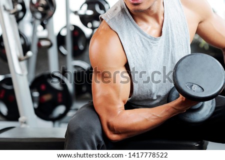 Fit strong man doing biceps curl in gym