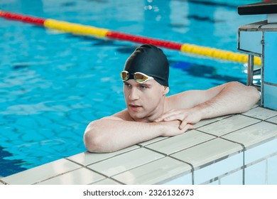 Fit strong swimmer with a black swimming cap looking at the pool, deep focusing on the race with swimming goggles. - Powered by Shutterstock