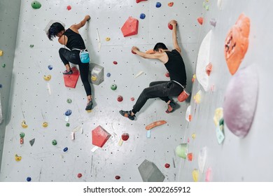 Fit Strong Young Couple Climbing Up Together On Buildering Wall When Training For Competition