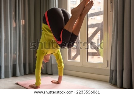 Fit strong young female in sportswear performing Bakasana pose while practicing yoga on mat near window at home