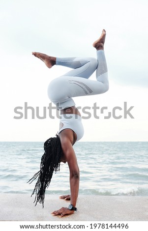 Fit strong young sportswoman doing handstand on embarkment with beautiful sea in background