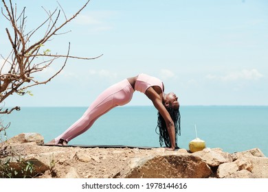 Fit strong young woman doing upward bow pose when working out on beach in the morning