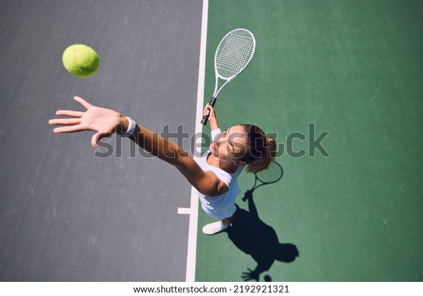 Fit tennis player, sport and serving during\
training, workout and exercise or match, game and competition from\
above. Sporty, active and healthy woman throwing a ball and\
practicing serve with