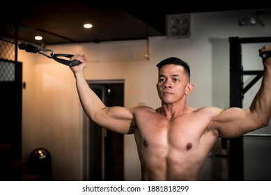 A Fit And Toned Asian Man With A Serious And Determined Look While Working Out, Doing Standing Cable Double Bicep Curls At The Gym.