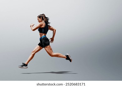 Fit white woman athlete in black sport bra and shorts running exercise. Fit American woman running. White woman athlete running against gray background. Studio photo of fit white woman running  - Powered by Shutterstock