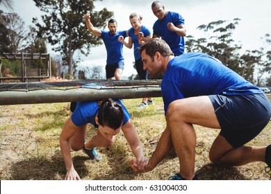 Fit woman crawling under the net during obstacle course while fit people cheering in bootcamp - Powered by Shutterstock