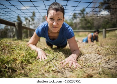 Fit woman crawling under the net during obstacle course in boot camp - Powered by Shutterstock