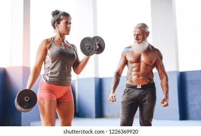 Fit woman doing curl biceps exercise with dumbbells in fitness gym center - Female athlete training with her personal trainer inside wellness sport club - Workout and sportive motivation concept  - Powered by Shutterstock