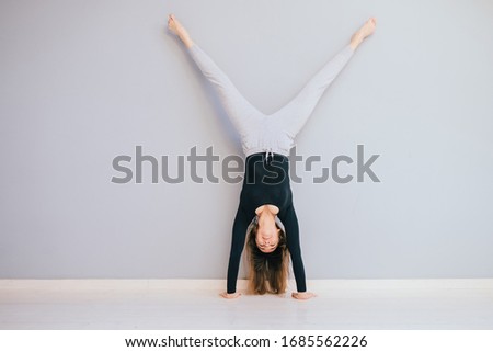 Fit woman doing handstand near empty grey wall at home. Athlete standing on hands Concept balance sport fitness