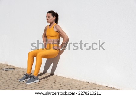 Fit woman doing squat exercise against a wall