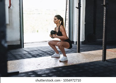 Fit woman doing squats with kettlebell in sport club, side view - Powered by Shutterstock