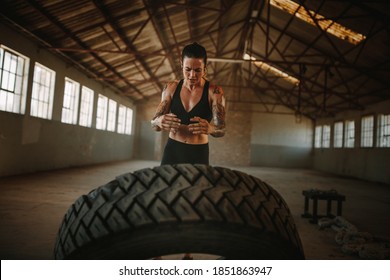 Fit Woman Doing Tire Flip Workout. Female In Sportswear Tossing A Tyre During An Intense Workout Session In An Empty Warehouse.