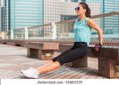 Fit woman doing triceps bench dips exercise while listening to music in headphones. Fitness girl working out in the city