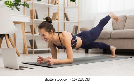 Fit woman doing yoga plank and watching online tutorials on laptop, training in living room - Shutterstock ID 1591188538