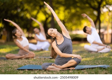 Fit woman enjoying group yoga session in peaceful setting of verdant summer park, performing stretches in lotus position while sitting on exercise mat.. - Powered by Shutterstock