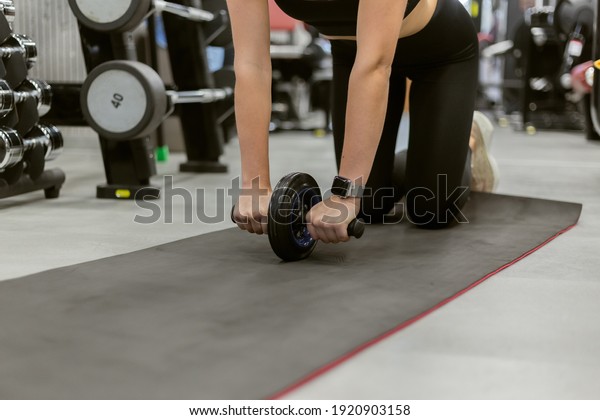 Fit woman\
exercising with ab wheel in modern\
gym
